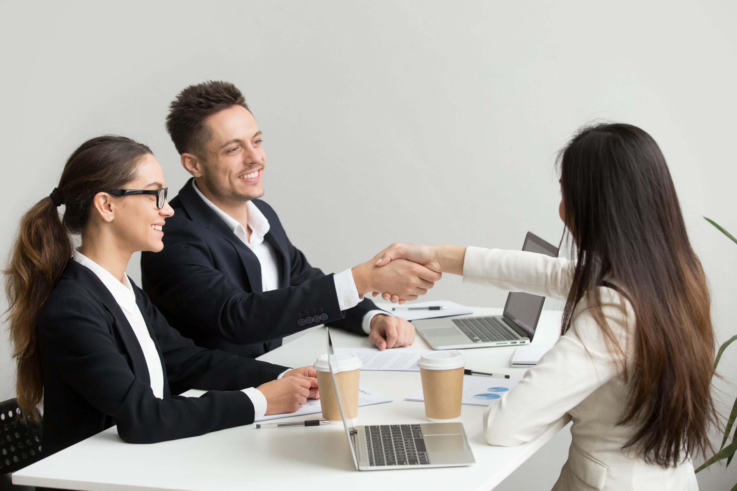 Friendly partners handshaking at group meeting thanking for succ Friendly satisfied partners handshaking at group meeting thanking for successful teamwork, smiling millennial businessman shaking hand greeting businesswoman, respect or making contract deal concept
